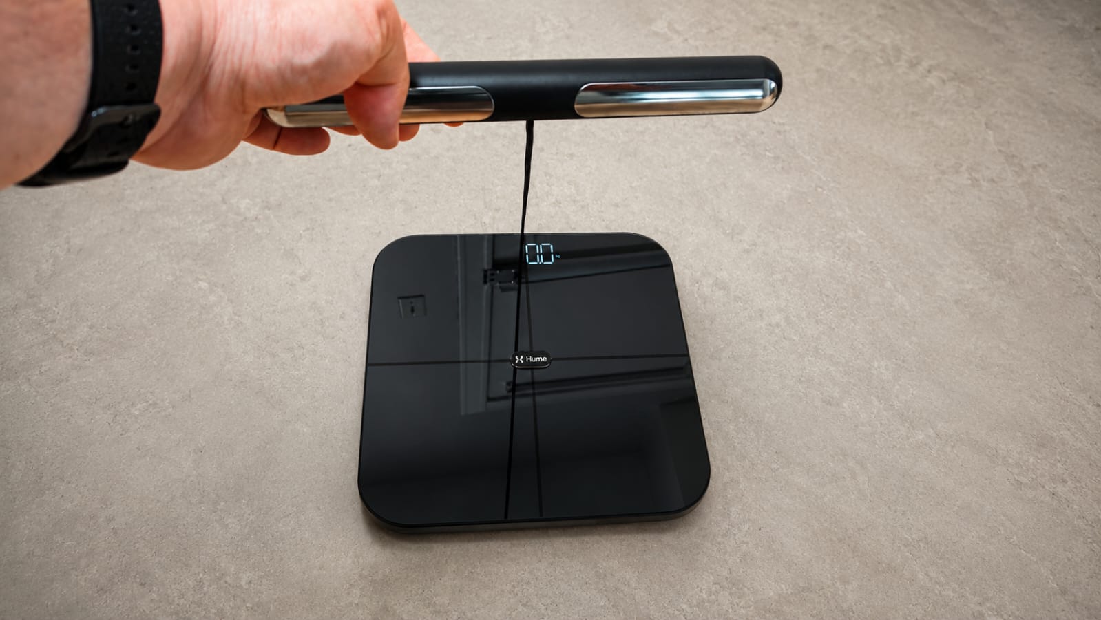 Hand holding the Hume Pod's handheld sensor bar over the scale